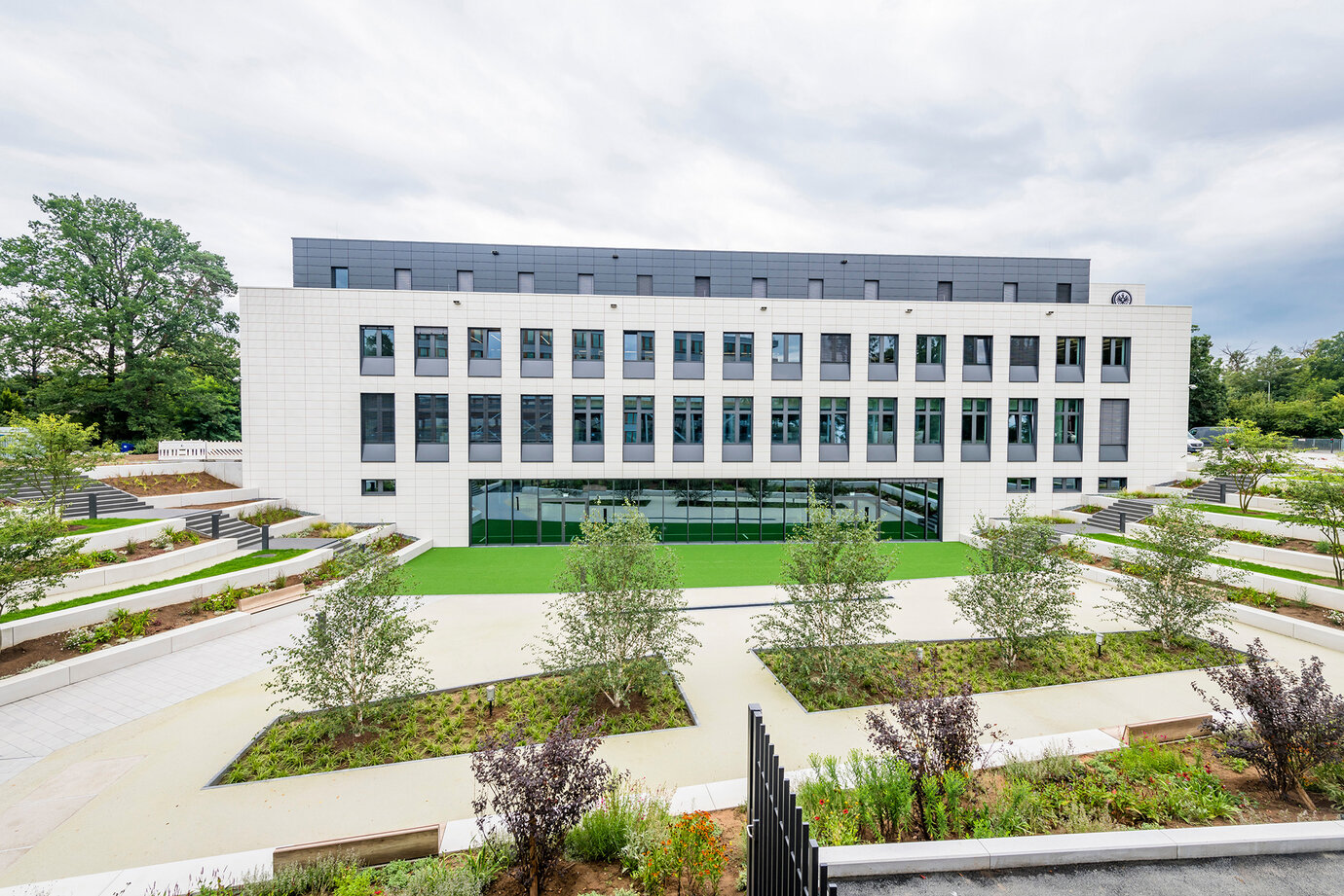 Von grünen Terrassen eingefasster Tiefhof, grüner Kunstrasenbelag erweitert das Fitness-Studio im UG in den Außenbereich
